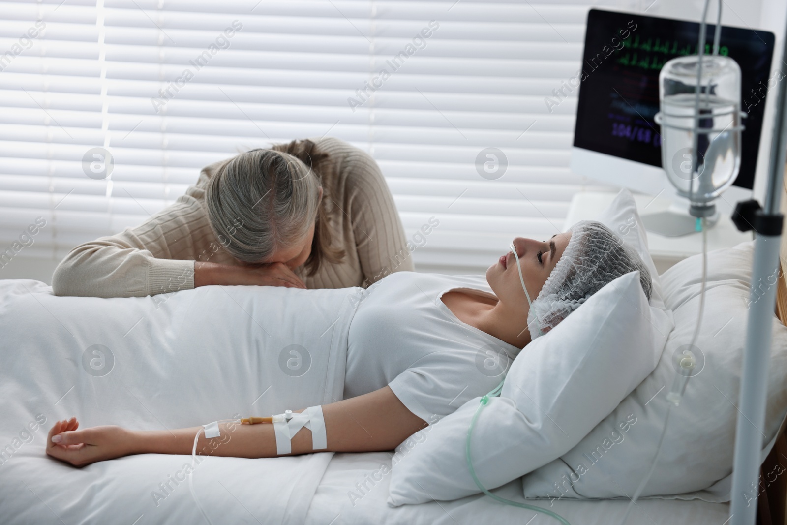 Photo of Coma patient. Sad mature woman near her unconscious daughter in hospital