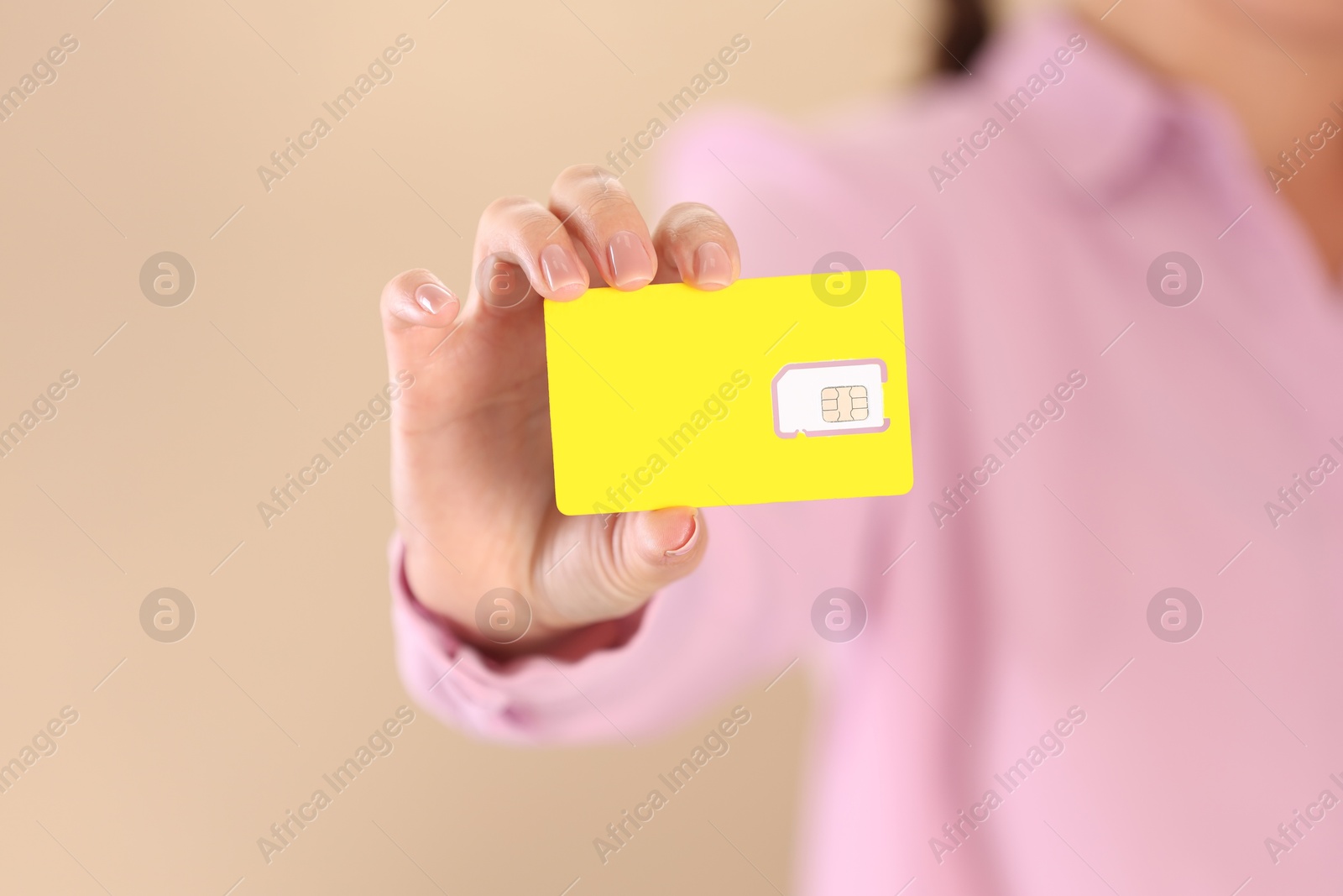 Photo of Woman holding SIM card on beige background, closeup