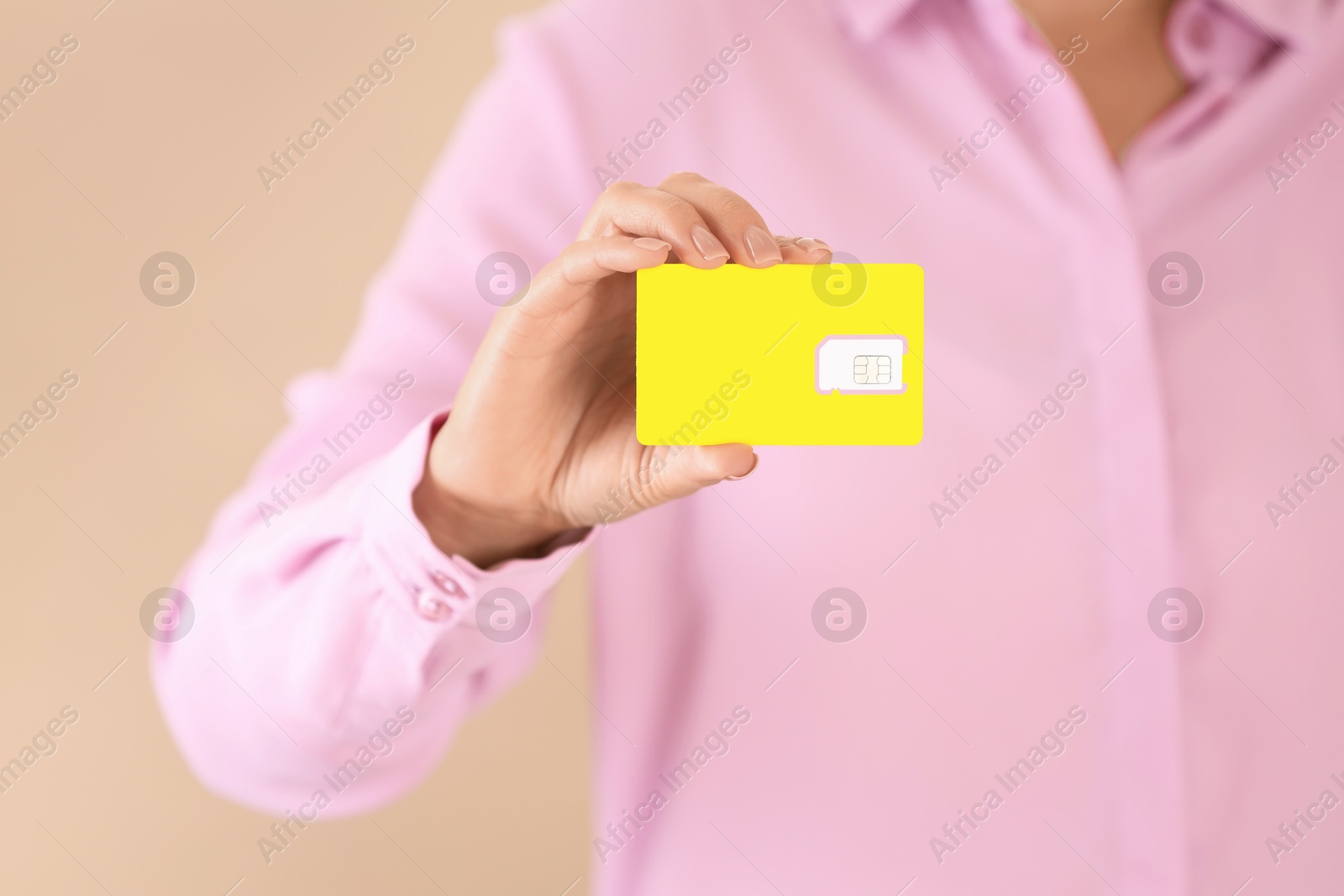 Photo of Woman holding SIM card on beige background, closeup