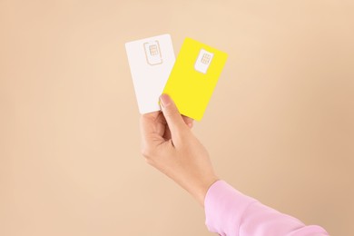 Photo of Woman holding SIM cards on beige background, closeup