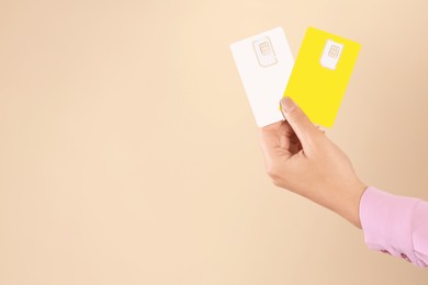 Photo of Woman holding SIM cards on beige background, closeup. Space for text