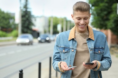Photo of Happy man with SIM card and smartphone outdoors, space for text