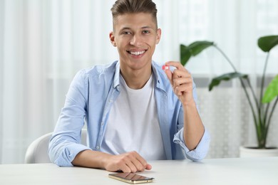 Photo of Man holding SIM card at white table with smartphone indoors
