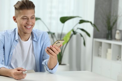 Photo of Man with SIM card and smartphone at white table indoors, space for text