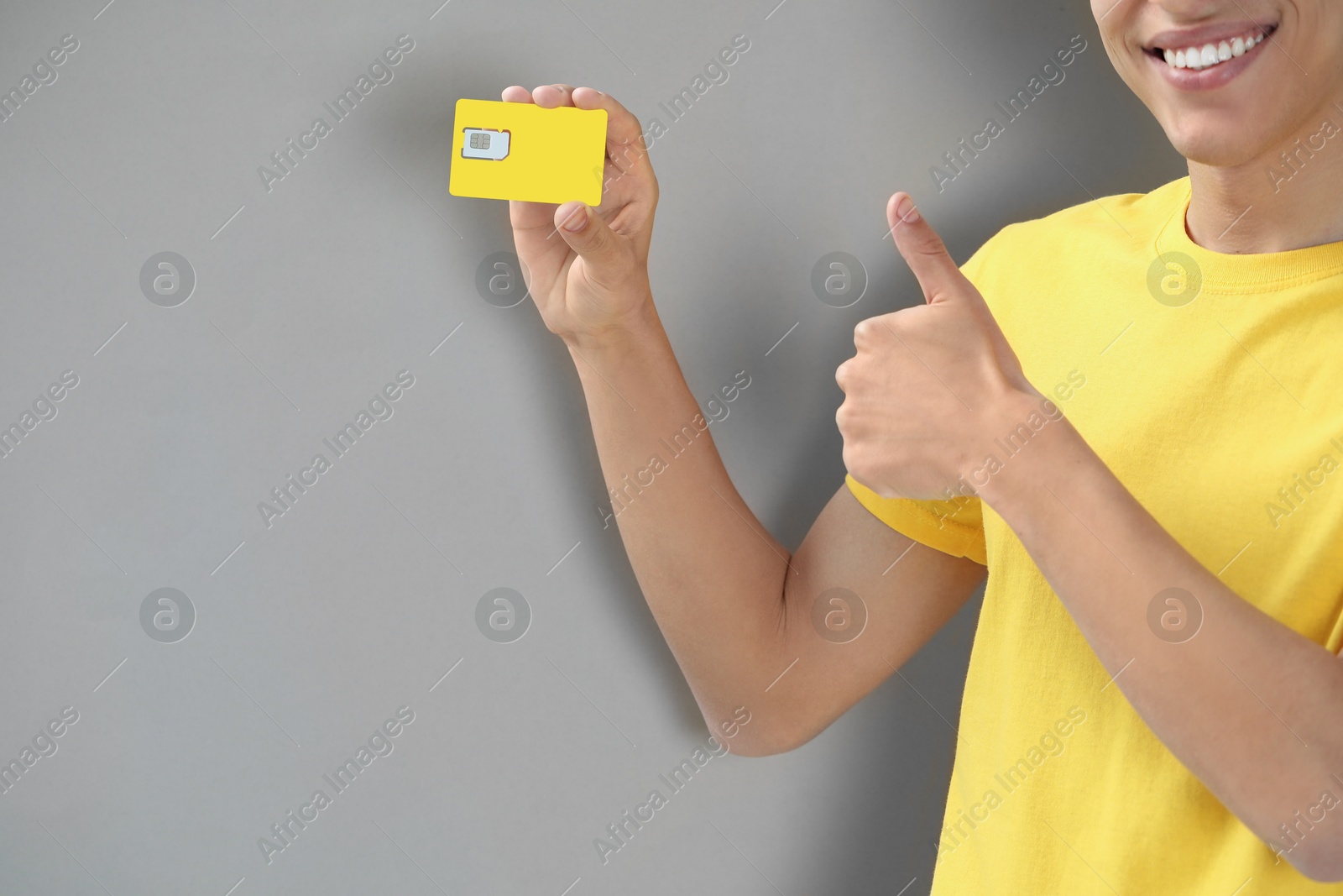 Photo of Man with SIM card showing thumbs up on grey background, closeup. Space for text