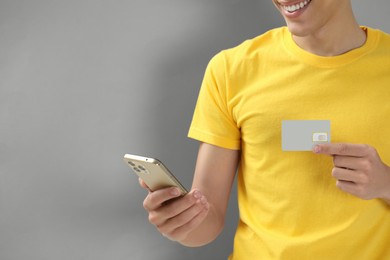 Photo of Man holding SIM card and smartphone on grey background, closeup. Space for text