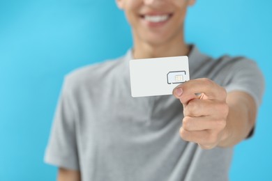 Photo of Man with SIM card on light blue background, closeup