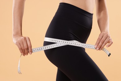 Photo of Diet and weight loss concept. Woman with measuring tape showing her slim body against beige background, closeup