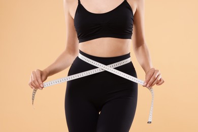 Photo of Diet and weight loss concept. Woman with measuring tape showing her slim body against beige background, closeup