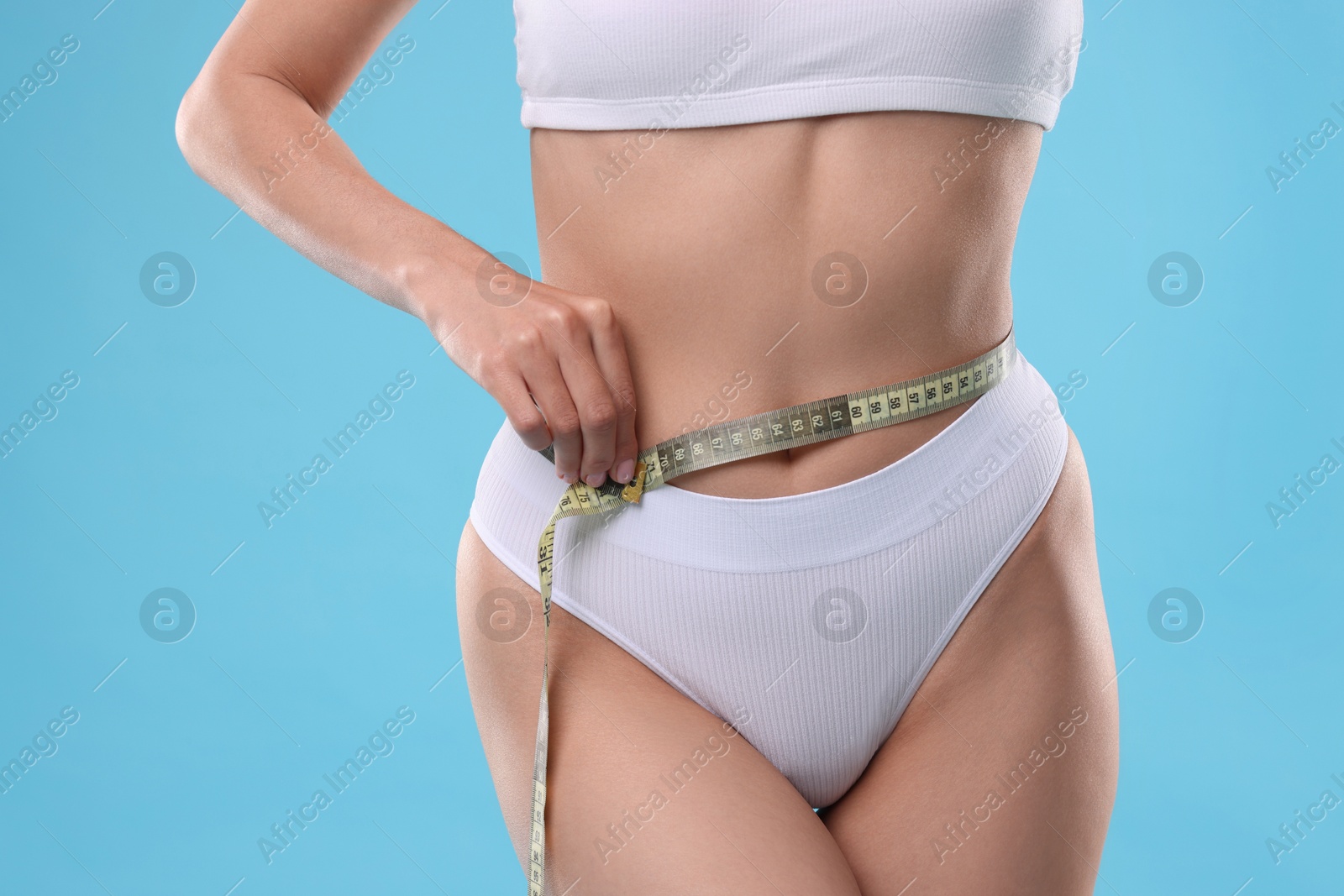 Photo of Diet and weight loss concept. Woman with measuring tape showing her slim body against light blue background, closeup