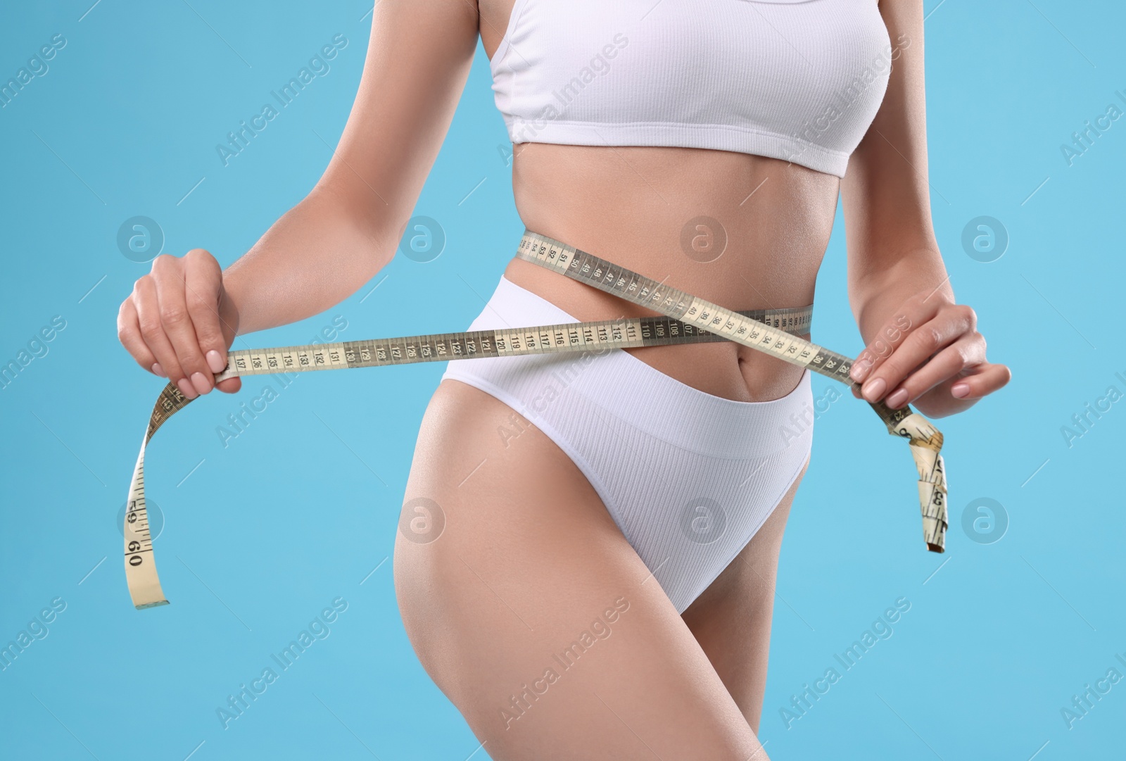 Photo of Diet and weight loss concept. Woman with measuring tape showing her slim body against light blue background, closeup