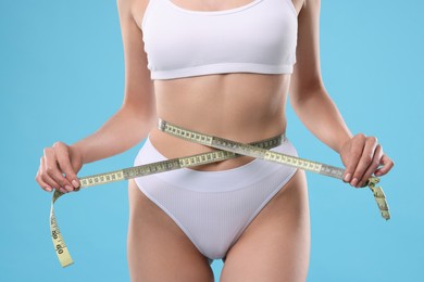 Photo of Diet and weight loss concept. Woman with measuring tape showing her slim body against light blue background, closeup