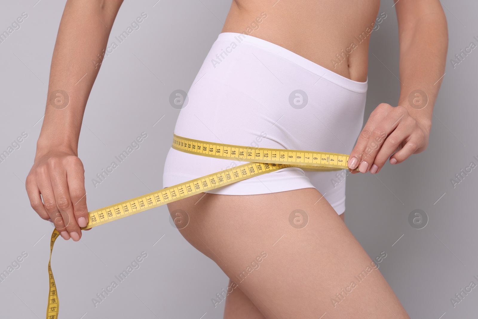 Photo of Diet and weight loss concept. Woman with measuring tape showing her slim body against light grey background, closeup