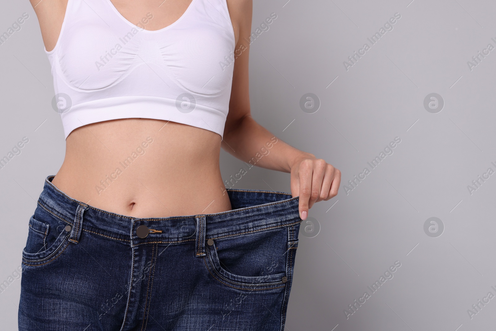 Photo of Diet and weight loss concept. Woman in big jeans showing her slim body on white background, closeup. Space for text