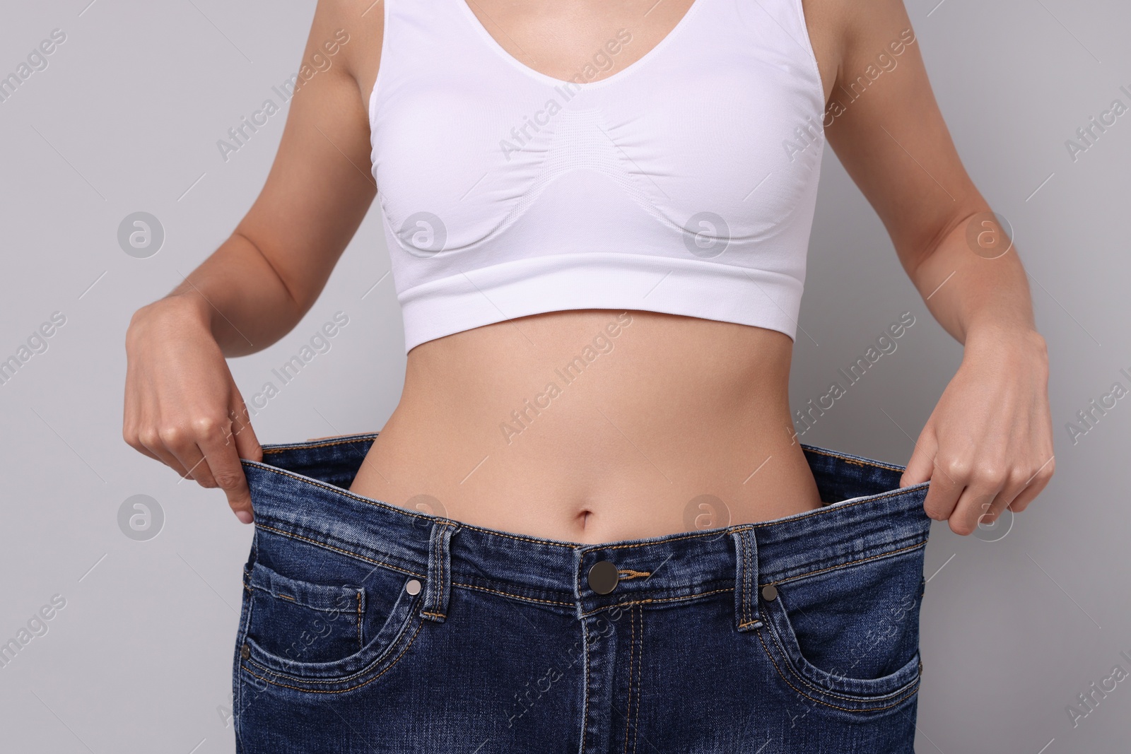 Photo of Diet and weight loss concept. Woman in big jeans showing her slim body on white background, closeup