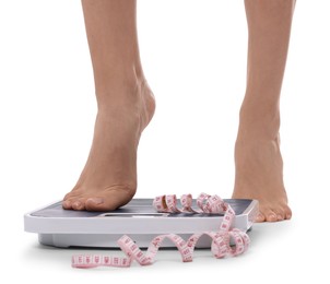 Photo of Diet and weight loss concept. Woman on floor scale and measuring tape against white background, closeup