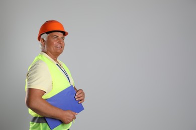 Photo of Engineer in hard hat with clipboard on grey background, space for text