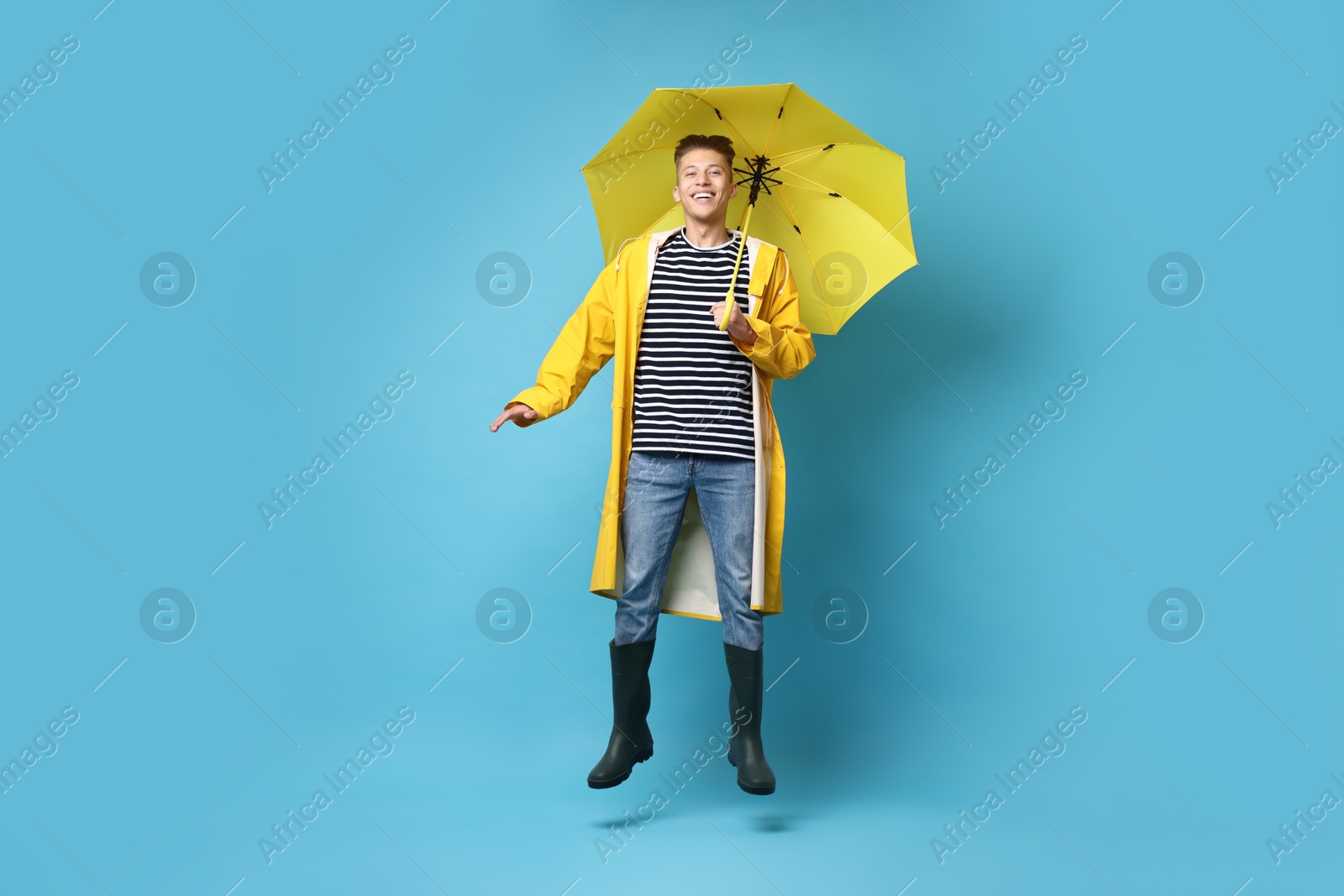 Photo of Young man with yellow umbrella jumping on light blue background