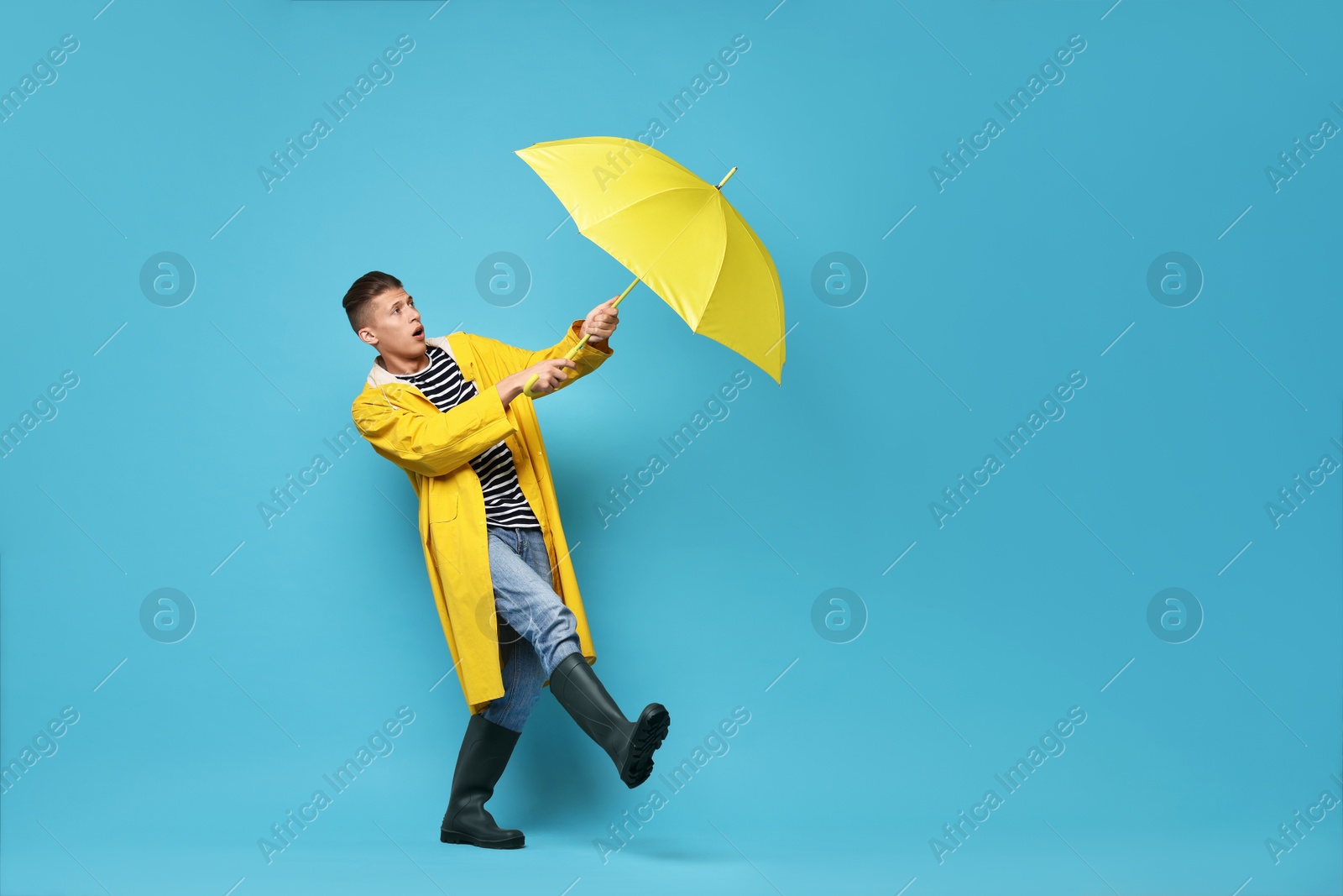 Photo of Young man with yellow umbrella on light blue background, space for text