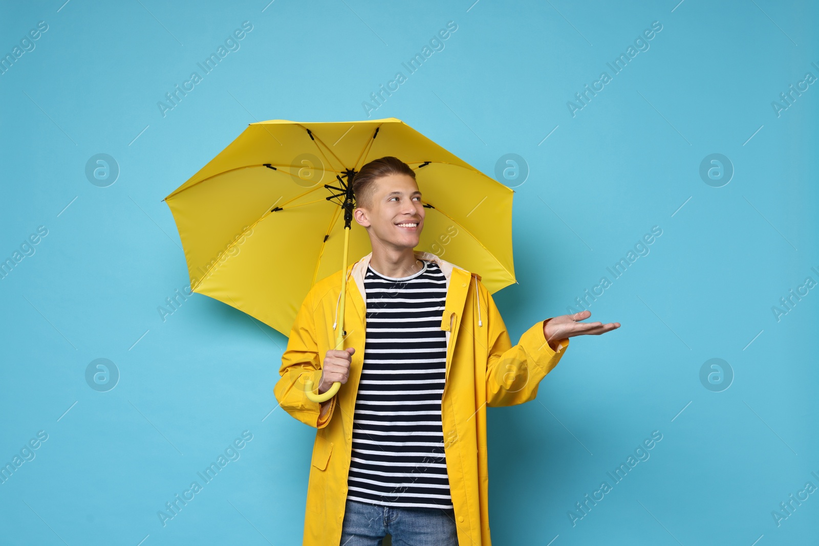 Photo of Young man with yellow umbrella on light blue background