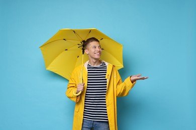 Young man with yellow umbrella on light blue background