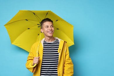 Photo of Young man with yellow umbrella on light blue background, space for text