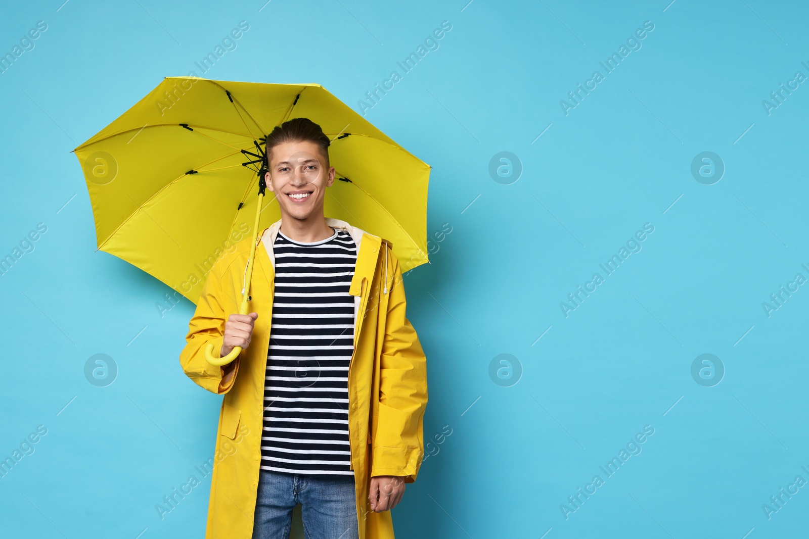 Photo of Young man with yellow umbrella on light blue background, space for text