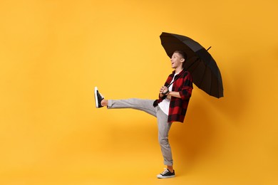 Photo of Young man with black umbrella on yellow background, space for text