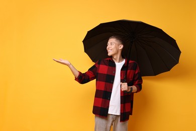 Photo of Young man with black umbrella on yellow background, space for text