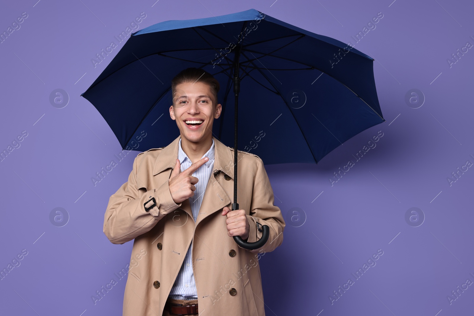 Photo of Young man with blue umbrella on purple background