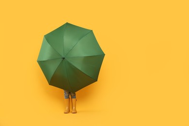 Photo of Little girl with green umbrella on yellow background. Space for text