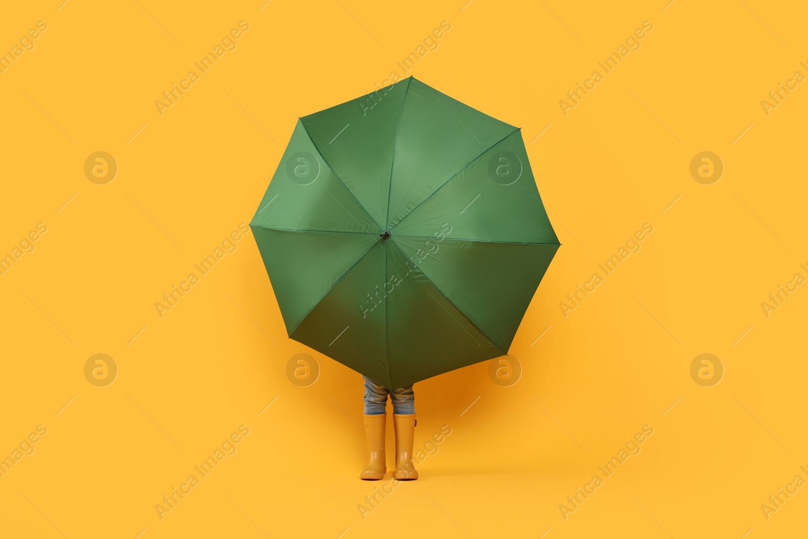 Photo of Little girl with green umbrella on yellow background