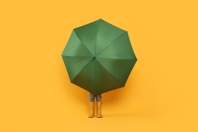 Little girl with green umbrella on yellow background