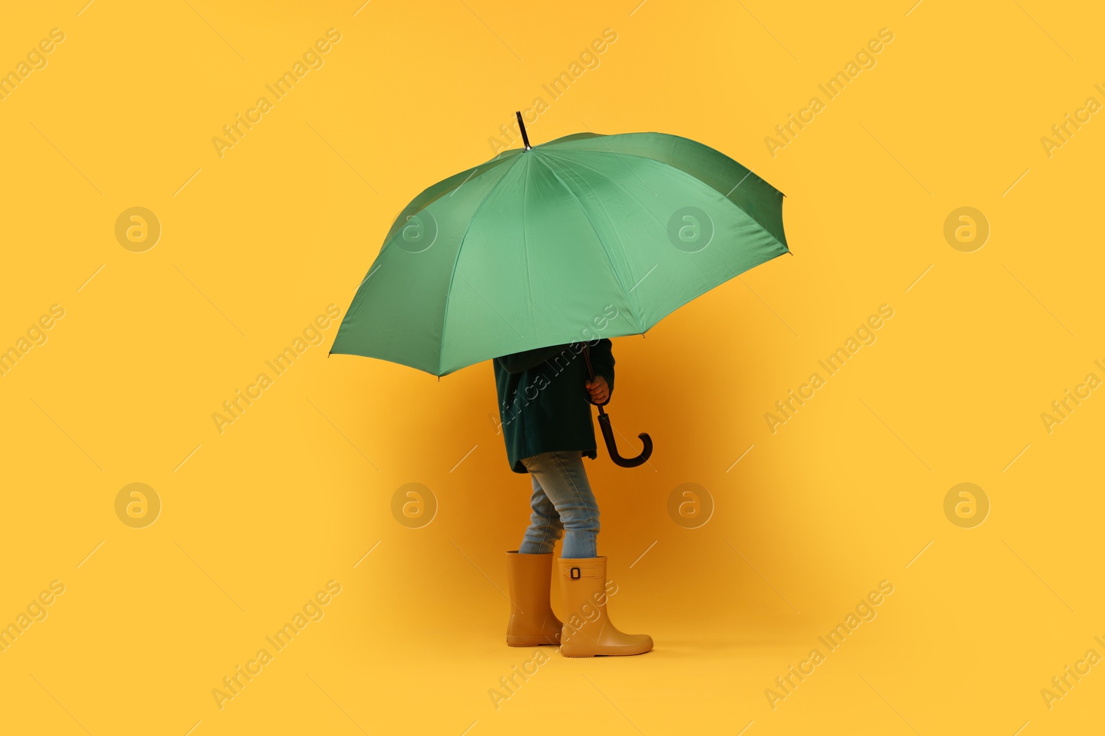 Photo of Little girl with green umbrella on yellow background