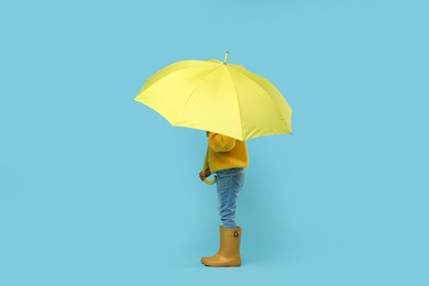 Photo of Little girl with yellow umbrella on light blue background