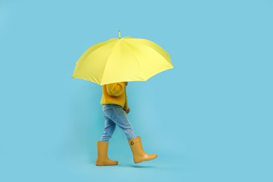 Photo of Little girl with yellow umbrella on light blue background