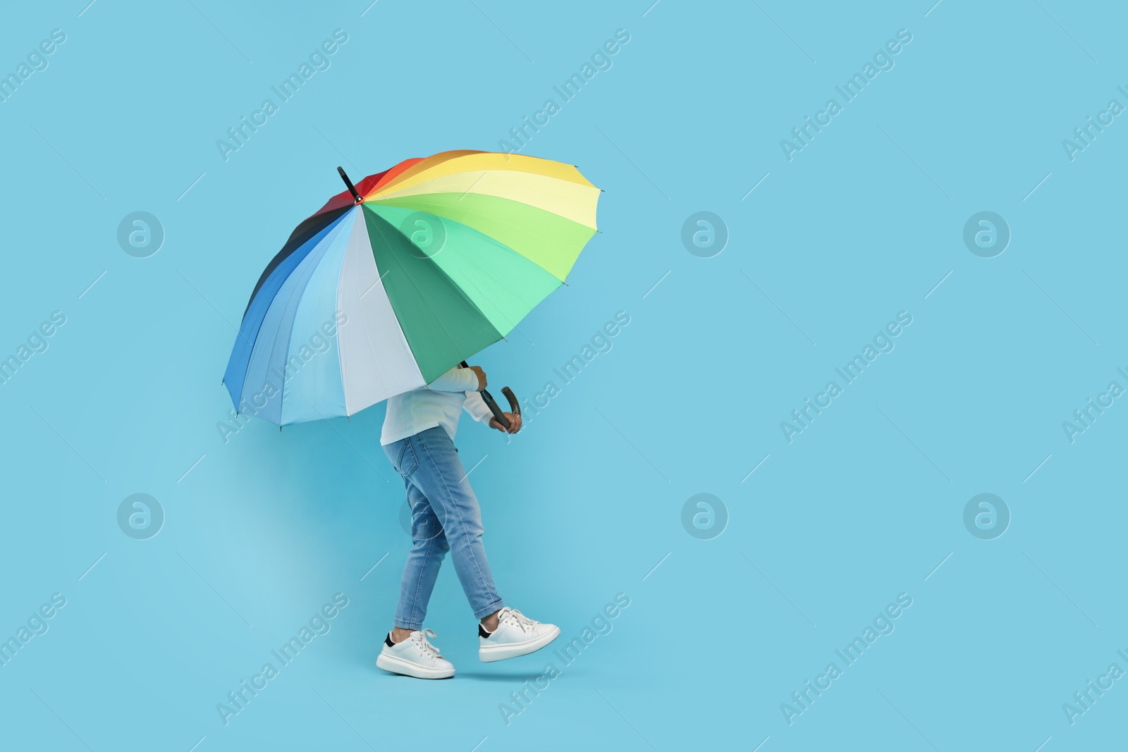 Photo of Little girl with colorful umbrella on light blue background. Space for text