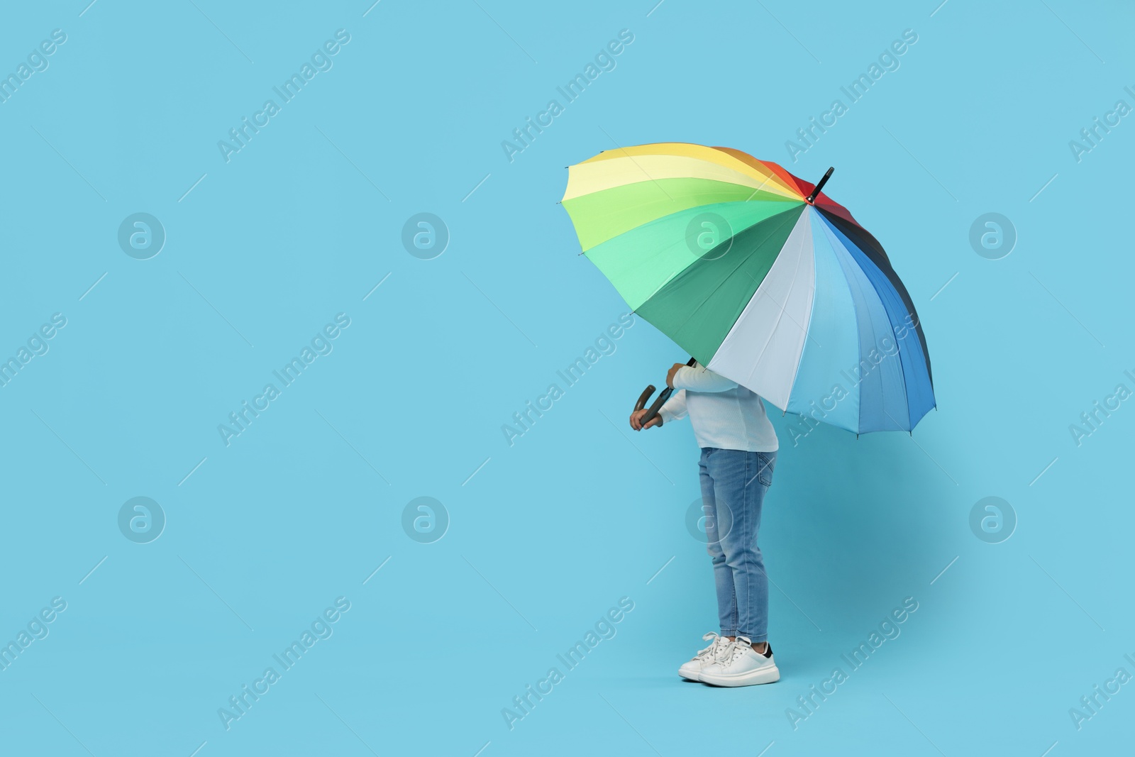 Photo of Little girl with colorful umbrella on light blue background. Space for text