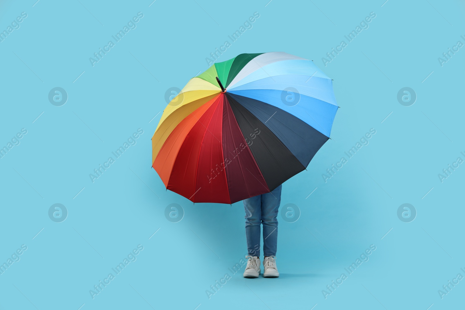 Photo of Little girl with colorful umbrella on light blue background. Space for text