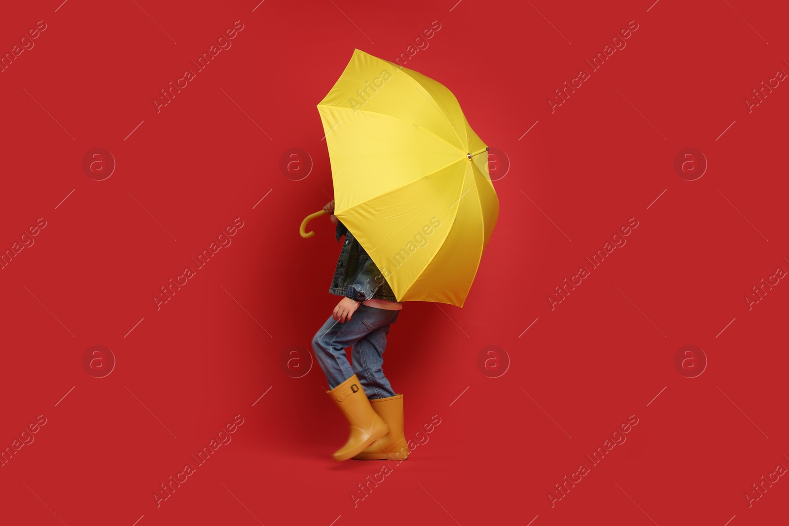 Photo of Little boy with yellow umbrella on red background