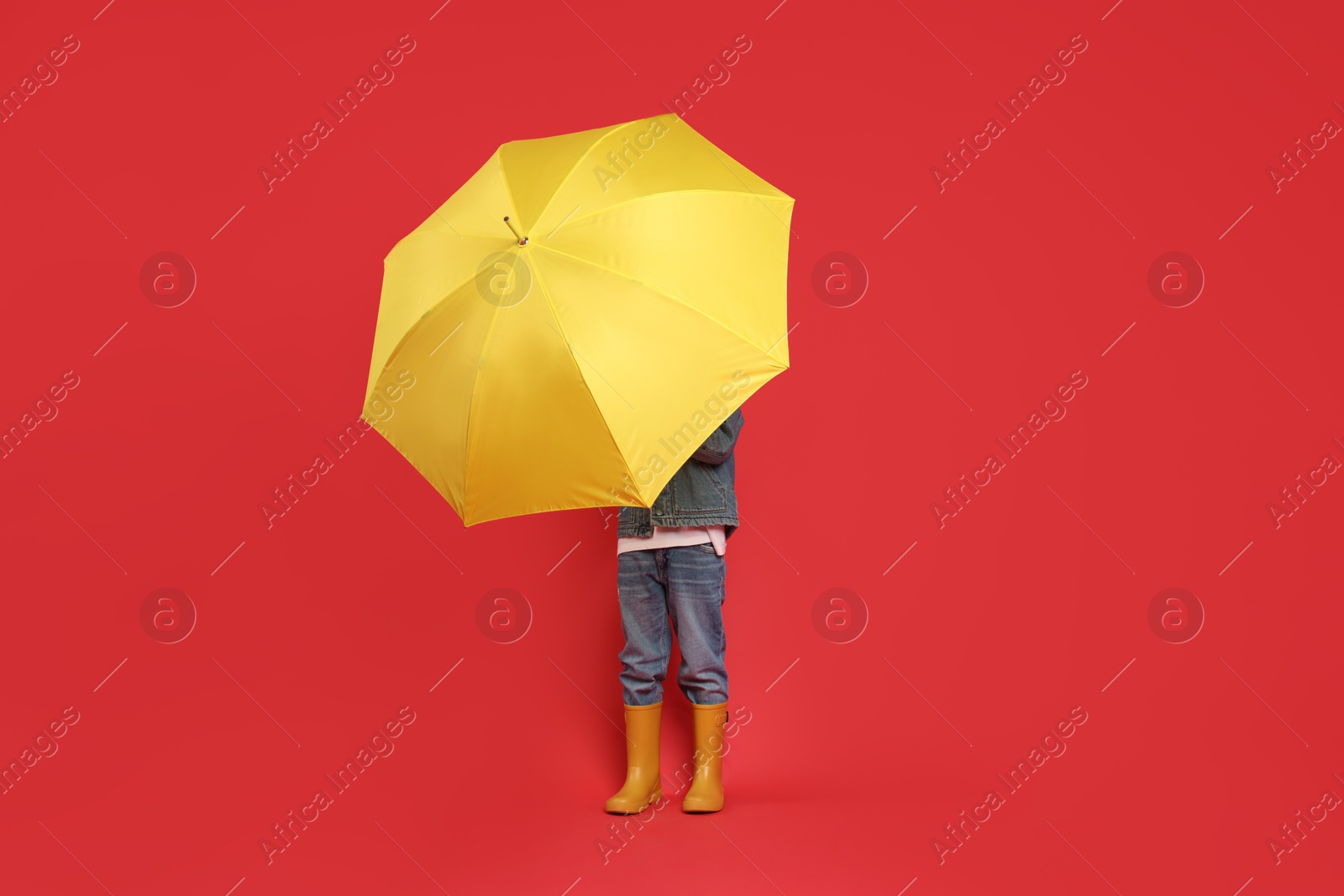 Photo of Little boy with yellow umbrella on red background, space for text