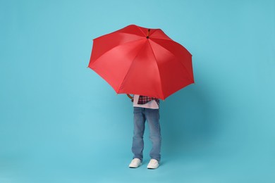 Little boy with red umbrella on light blue background