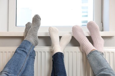 Family warming feet near heating radiator at home, closeup