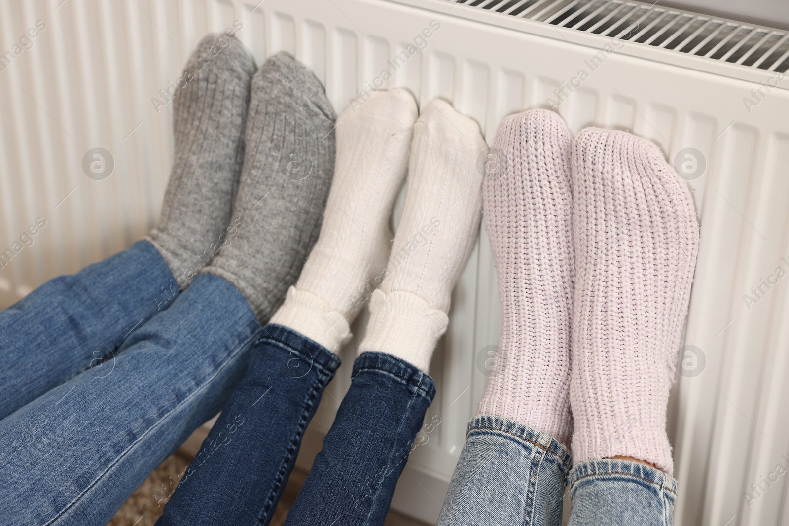 Photo of Family warming feet near heating radiator at home, closeup