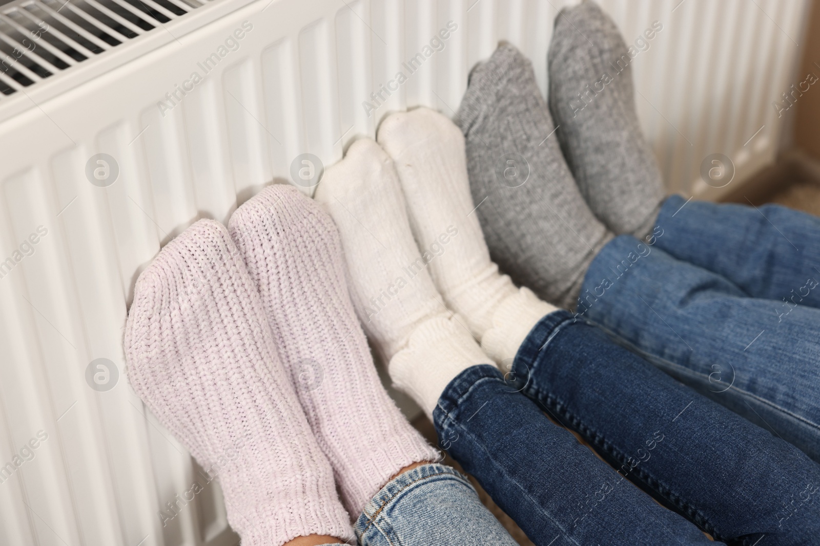 Photo of Family warming feet near heating radiator at home, closeup