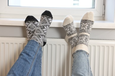 Photo of Couple warming feet near heating radiator at home, closeup