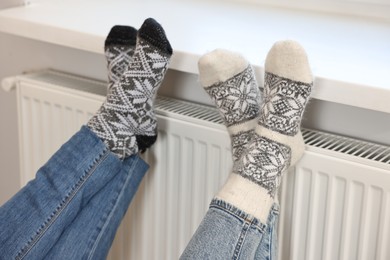 Photo of Couple warming feet near heating radiator at home, closeup