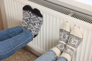 Couple warming feet near heating radiator at home, closeup