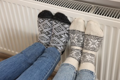Photo of Couple warming feet near heating radiator at home, closeup