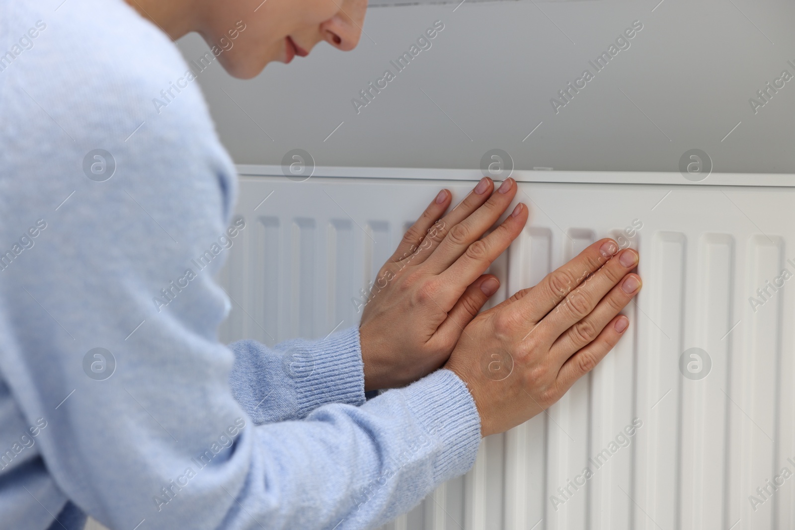 Photo of Woman warming hands near heating radiator indoors, closeup